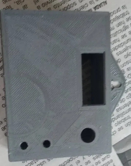 Caja impresa en 3D gris, cerrada, con una ventana rectangular para la pantalla OLED, dos agujeros pequeños para los LED y uno grande abajo