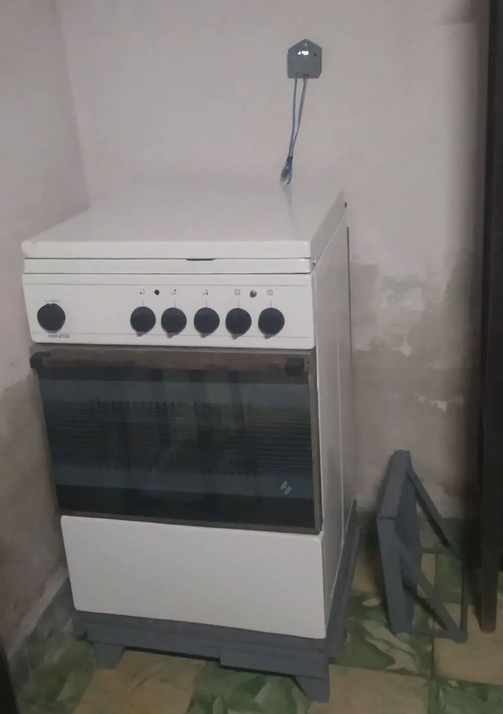 Cocina eléctrica blanca arrimada a una esquina y, atornillada a la pared justo encima, la caja gris impresa en 3D del controlador, con un par de cables azules bajando de ella