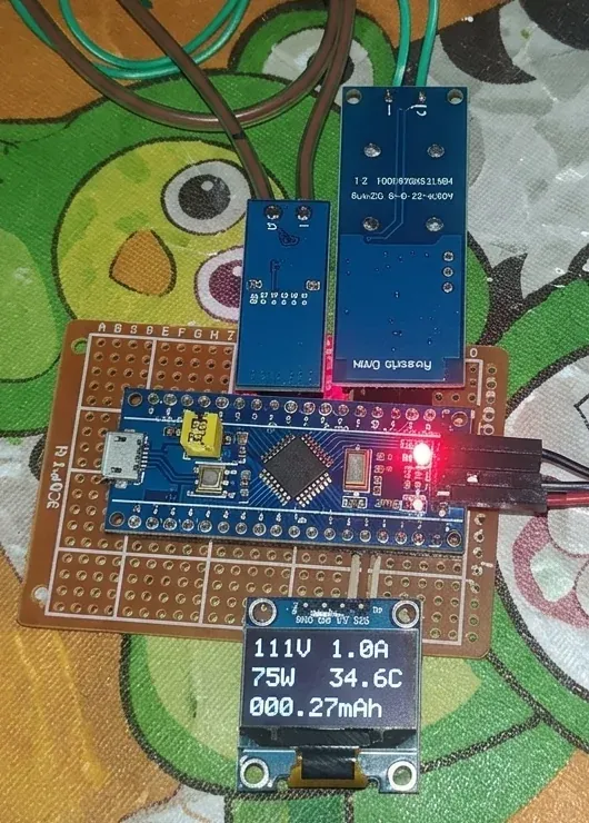 Placa STM32 y dos módulos montados sobre una placa perforada, con una pantalla OLED encendida que muestra 111 V, 1.0 A, 75 W, 34.6 C y 000.27 mAh