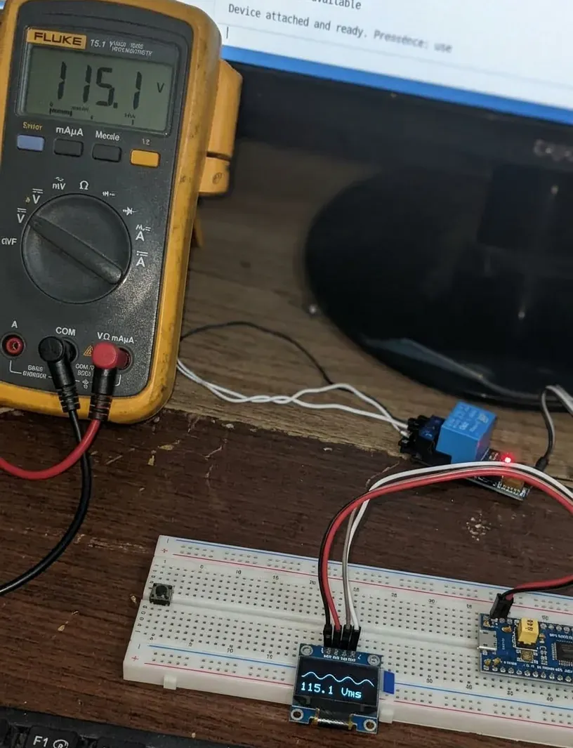 Un multímetro Fluke marca 115.1 V y, al lado, el medidor sobre protoboard muestra en su pantalla OLED la misma cifra, 115.1 Vrms, con la forma de onda de la red dibujada encima