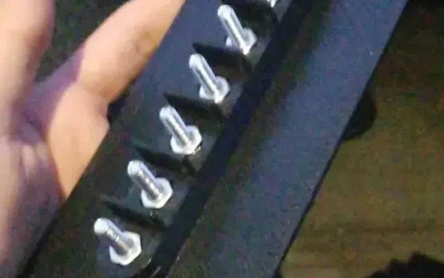 Mano señalando los puntos de fijación impresos en 3D de un compartimento de doble fondo, con espárragos que sobresalen