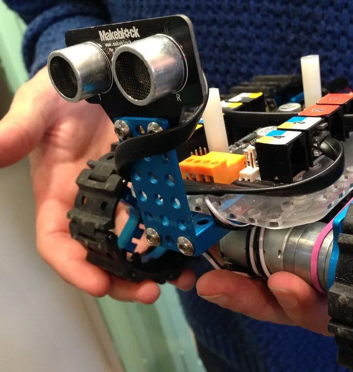 Manos sosteniendo un pequeño robot con sensor ultrasónico, motores y orugas