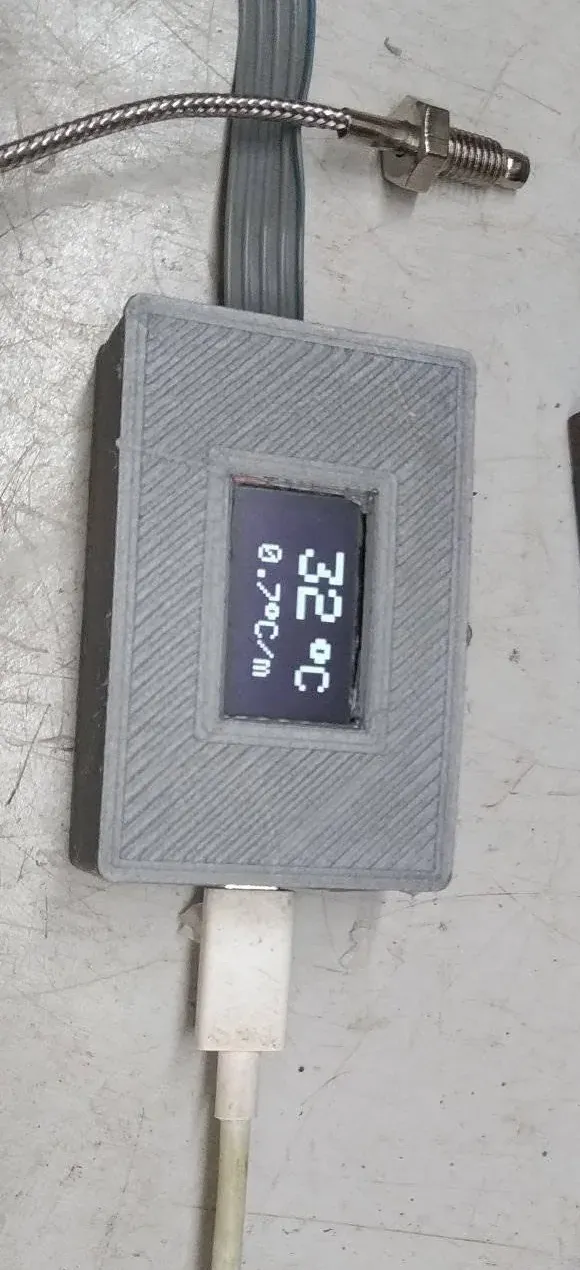 Caja impresa en 3D cerrada con la pantalla OLED marcando 32 grados Celsius y, al lado, 0,7 grados Celsius por minuto; arriba, el termopar con su sonda de rosca y el cable trenzado